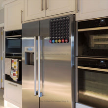 Black magnetic Dolce Gusto coffee pod capsule holder shown installed on fridge freezer in kitchen.